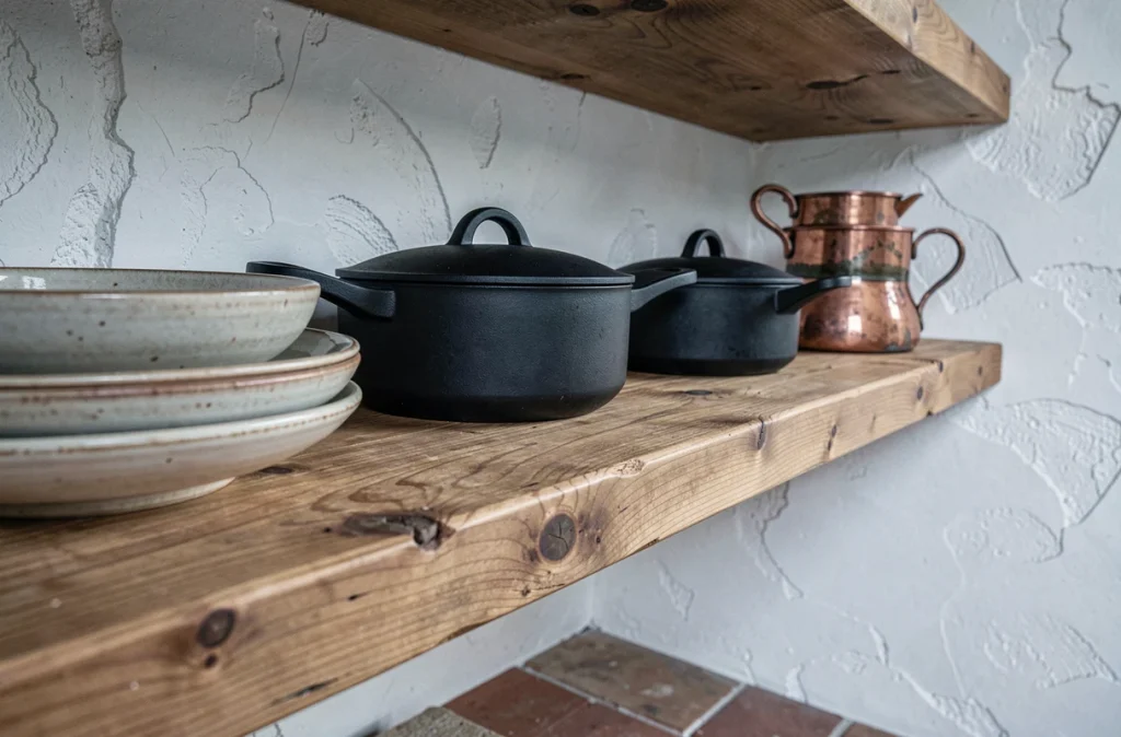 Étagère en châtaignier patiné dans un mas provençal avec batterie de cuisine moderne en fonte noire et vaisselle artisanale en grès
